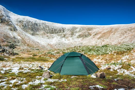 Green tent in snow mountains. Beautiful spring landscape