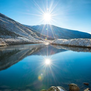 Beautiful blue lake in the mountains, morning sunrise time. Landscape with snow shining sun