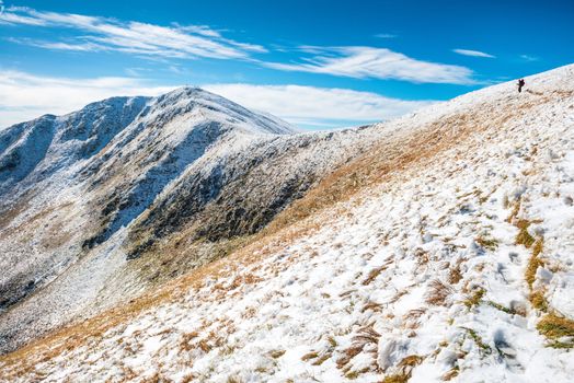 White peaks of mountains in snow and man hiking along winter landscape