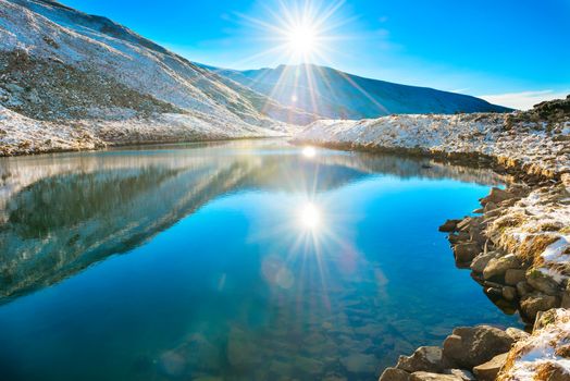 Beautiful blue lake in the mountains, morning sunrise time. Landscape with snow shining sun