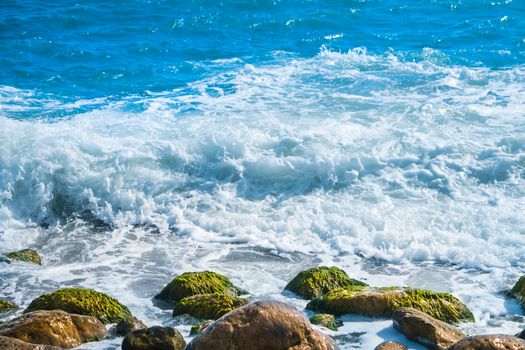 Sea coast with stones, surfing wave on the background