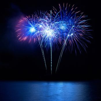 Blue fireworks above water with reflection on the black sky background