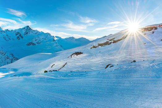 Sunset in winter mountains covered by snow. Ski slope and shining sun on the blue sky