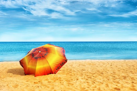 Orange umbrella on golden sand beach in a sunny day, blue sea in background