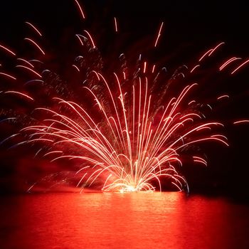 Red holiday fireworks on the lake with black sky background