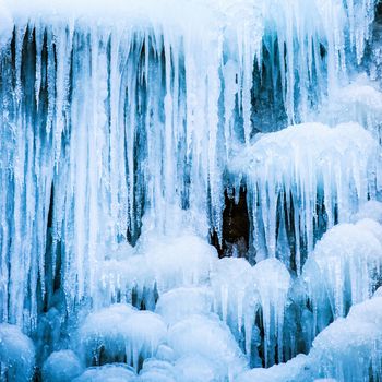 Frozen ice waterfall of blue icicles on the rock