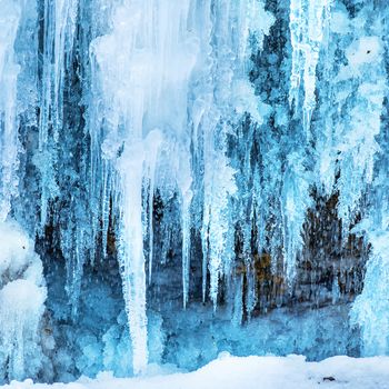 Frozen ice waterfall of blue icicles on the rock