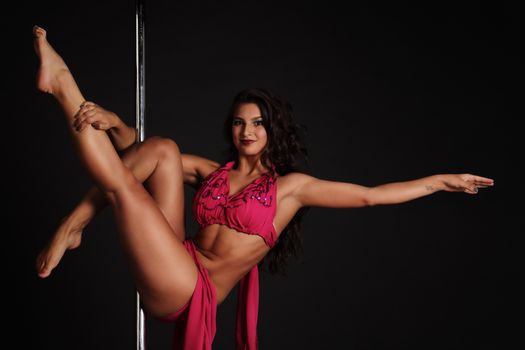 Beautiful woman performing pole dance on dark background
