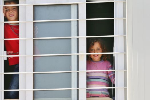 GREECE, Athens: Two shy children peer out the window of their prefabhome at Skaramagas camp, managed and supplied by the Greek Army on April 14, 2016 in Athens, Greece.