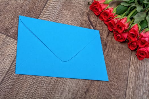 Blue envelope and red roses on a wooden background