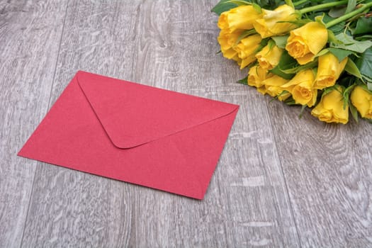 Red envelope and yellow roses on a wooden background