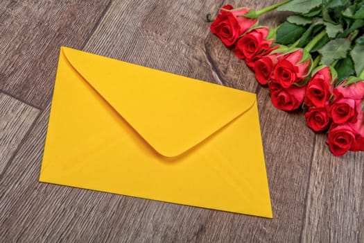 Yellow envelope and red roses on a wooden background