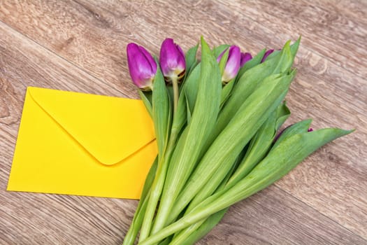 Envelope and violet tulips on a wooden background