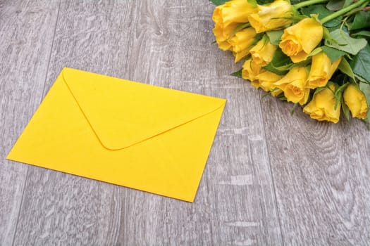 Yellow envelope and yellow roses on a wooden background