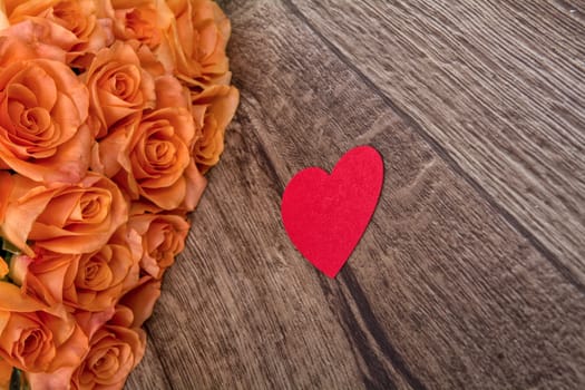 Orange roses and red heart on a wooden background