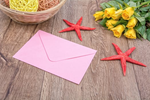 Envelope, red starfishes and roses on a wooden background