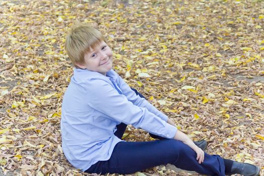 Cute blond boy sitting on autumn yellow foliage