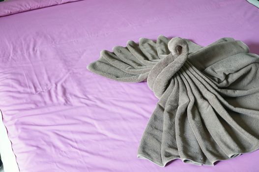 Brown towel plait as swan on purple bed in hotel room.
