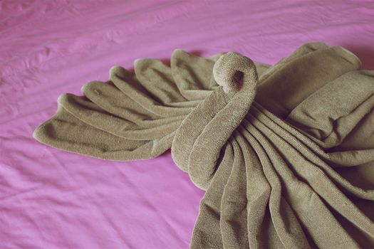 Close up brown towel plait as swan on purple bed in hotel room vintage style.