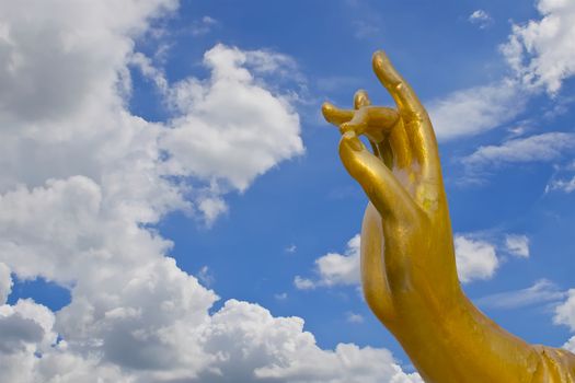 Golden hand of Guanyin statue with white cloud and blue sky.