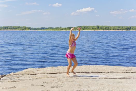 Dancing girl on the riverbank in pink swimsuit