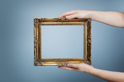 Man holding an antique style golden frame in his hands.