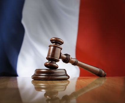 Mahogany wooden gavel on glossy wooden table, flag of France in the background.