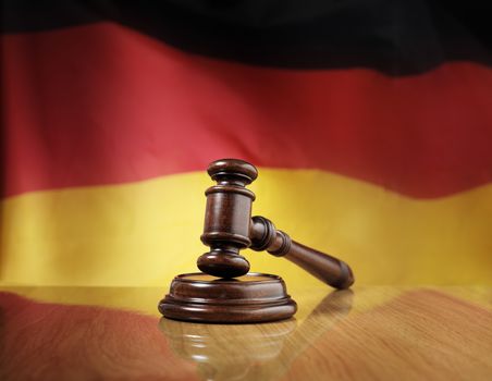 Mahogany wooden gavel on glossy wooden table, flag of Germany in the background.