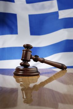 Mahogany wooden gavel on glossy wooden table, flag of Greece in the background.