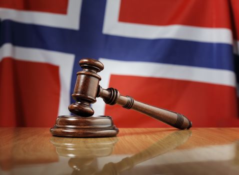 Mahogany wooden gavel on glossy wooden table, flag of Norway in the background.