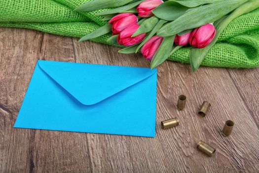Blue envelope, tulips and bullets on a wooden background