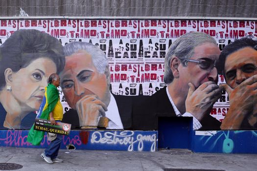 BRAZIl, Sao Paulo: A man holding a placard walks along a painted wall as thousands of activists supporting the impeachment of President Dilma Rousseff take part in a protest in Sao Paulo, on April 17, 2016. Brazilian lawmakers on Sunday reached the two thirds majority necessary to authorize impeachment proceedings against President Dilma Rousseff. The lower house vote sends Rousseff's case to the Senate, which can vote to open a trial. A two thirds majority in the upper house would eject her from office. Rousseff, whose approval rating has plunged to a dismal 10 percent, faces charges of embellishing public accounts to mask the budget deficit during her 2014 reelection.
