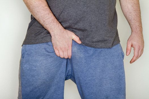 After a long workout a man is scratching his groin due to jock itch
