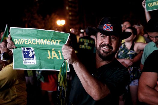 BRAZIL, Curitiba: A man holds a sign which reads Impeachment now! as activists supporting the impeachment of Brazilian President Dilma Rousseff follow on a big screen as lawmakers vote on whether the impeachment of Rousseff will move forward, in Curitiba, southern Brazil, on April 17, 2016. Brazilian lawmakers on Sunday reached the two thirds majority necessary to authorize impeachment proceedings against President Dilma Rousseff. The lower house vote sends Rousseff's case to the Senate, which can vote to open a trial. A two thirds majority in the upper house would eject her from office. Rousseff, whose approval rating has plunged to a dismal 10 percent, faces charges of embellishing public accounts to mask the budget deficit during her 2014 reelection.