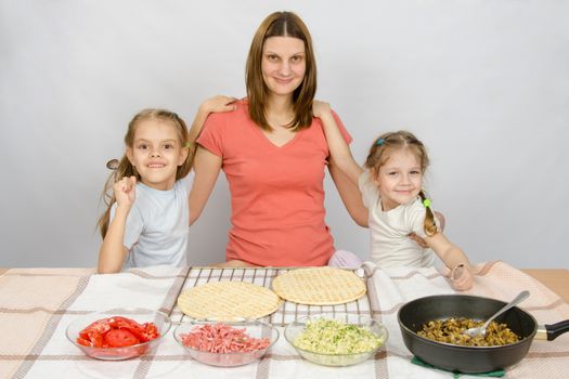 Mother with two daughters at the kitchen table are going to cook a pizza and a fun look into the frame