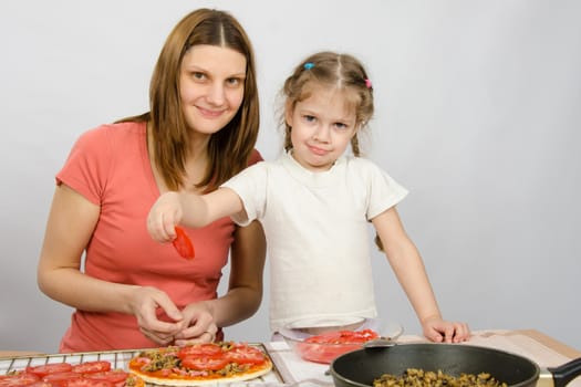 Little five-year girl helps mother spread on the pizza ingredients