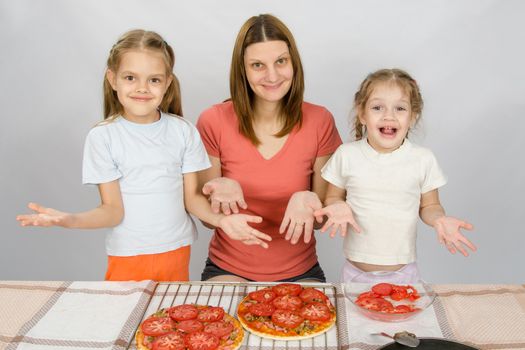 Mom with two young daughters happily show made pizza with tomatoes