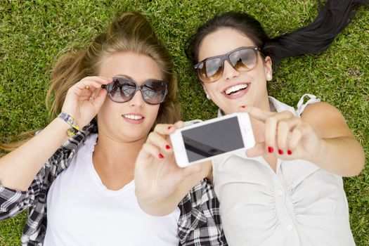 Female best friends lying on the grass and making selfies