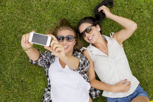 Female best friends lying on the grass and making selfies