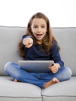 Happy little girl sitting on a couch and using a tablet