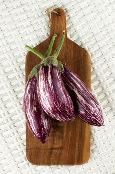 Three Fresh Raw Striped Aubergines on Wooden Cutting Board closeup on Wicker background. Top View