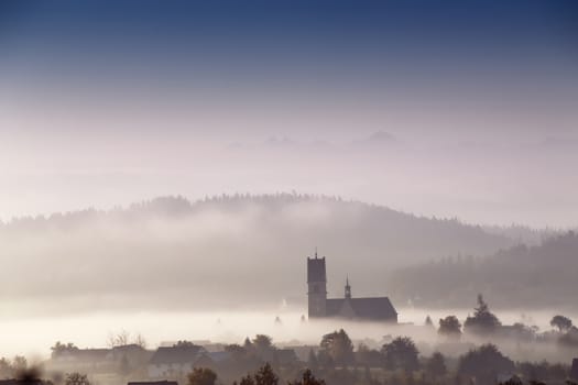 Foggy morning in small town. Church in a mist. Poland (malopolska) autumn sunny morning.