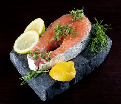 Perfect Raw Salmon Steak with Lemon and Rosemary on Shale Stone Board closeup on Dark Wooden background