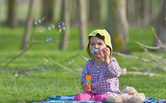 little girl is blowing a soap bubbles in forest