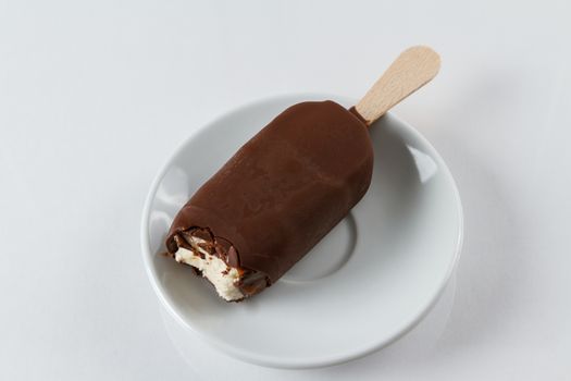 A still frozen chocolate covered vanilla popsicle with raspberry filling, with a bite already taken out of it