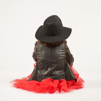 Little girl with black hat sitting and pouting. Back view