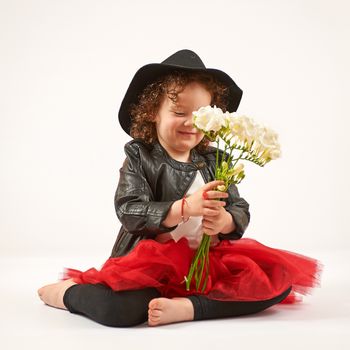 Little girl with black hat sitting and admiring flowers