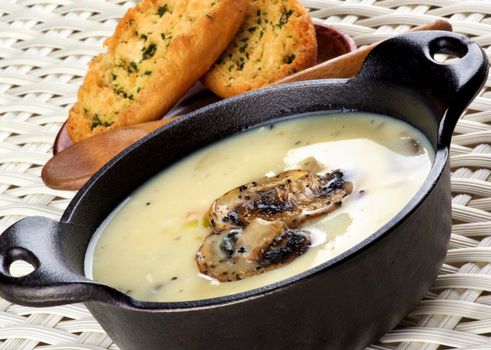 Delicious Homemade Mushrooms Cream Soup Decorated with Roasted Champignons in Black Iron Stewpot with Garlic and Herb Crunchy Bread closeup on Wicker background