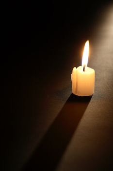 One lighting candle with long shadow on dark background