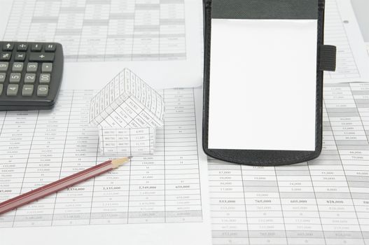 Notepad place vertical and brown pencil with house and calculator on finance account  as background.